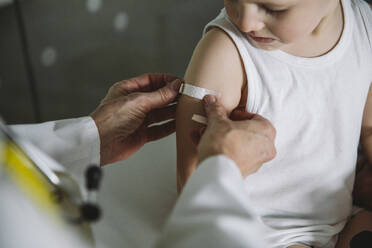 Kinderarzt klebt Pflaster auf den Arm eines Kleinkindes nach einer Impfung - MFF05526