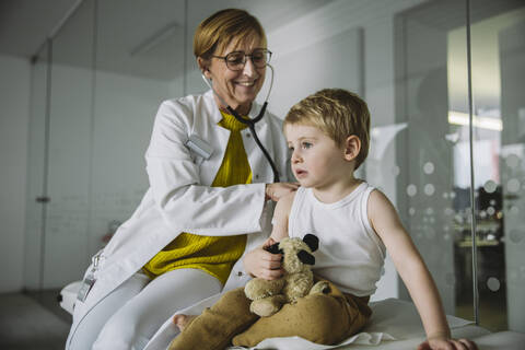Arzt untersucht ein Kleinkind mit einem Stethoskop, lizenzfreies Stockfoto