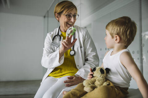 Kinderarzt mit Fingerpuppen und Kleinkind in der Arztpraxis, lizenzfreies Stockfoto