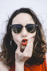 Porträt einer jungen Frau mit roten Lippen, die eine Sonnenbrille trägt und einen Schmollmund macht - FVSF00064