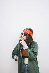 Porträt einer jungen Frau mit Stirnband und Sonnenbrille, die eine Karotte raucht - FVSF00073