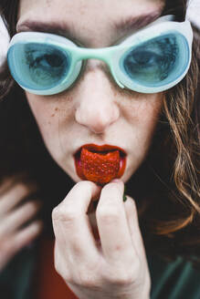 Porträt einer Frau mit blauer Taucherbrille, die eine Erdbeere isst - FVSF00078