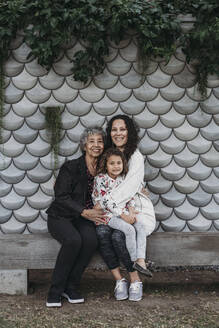 Porträt einer Mehrgenerationenfamilie, die draußen sitzt und lächelt - CAVF79015
