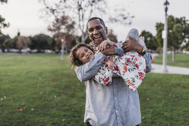 Glücklicher Vater hält süßes Mädchen im Park Spielplatz in der Abenddämmerung - CAVF79023
