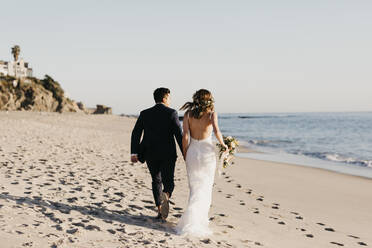 Rear view of happy bridal couple running at the beach - LHPF01253