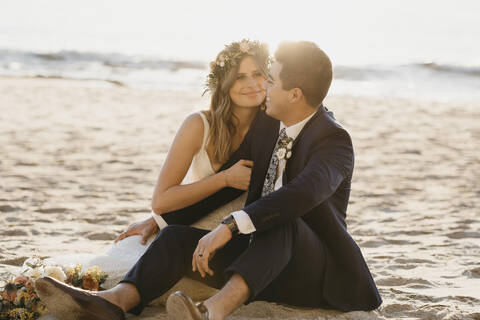 Glückliches Brautpaar am Strand sitzend, lizenzfreies Stockfoto