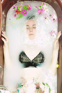 Woman wearing bra taking a milk bath with blossoms - ERRF03394