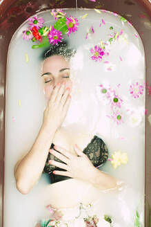 Woman wearing bra taking a milk bath with blossoms - ERRF03395