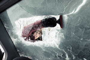 Porträt einer jungen Frau, die Schnee von der Windschutzscheibe eines Autos wischt - WFF00311
