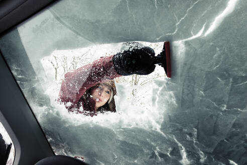 Portrait of young woman cleaning snow from car's windscreen - WFF00311