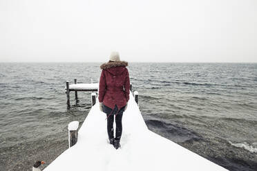 Back view of young woman standing on snow-covered jetty at Lake Starnberg, Germany - WFF00321