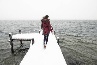 Rückenansicht einer jungen Frau, die auf einem schneebedeckten Steg am Starnberger See läuft, Deutschland - WFF00322