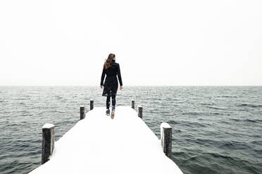 Rückenansicht einer jungen Frau, die auf einem schneebedeckten Steg am Starnberger See spazieren geht, Deutschland - WFF00325