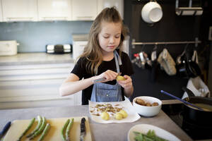 Porträt eines Mädchens, das in der Küche Kartoffeln schält - HMEF00871