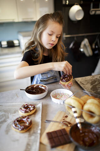 Porträt eines Mädchens, das selbstgebackene Krapfen mit Zuckerkörnern verziert, lizenzfreies Stockfoto