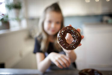 Girl presenting home-baked doughnut with chocolate icing and sugar granules, close-up - HMEF00875