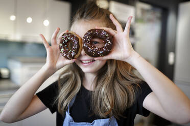 Portrait of smiling girl looking through doughnuts - HMEF00877