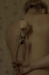 Rear view of nude woman lying in bed with dried flower - ERRF03399