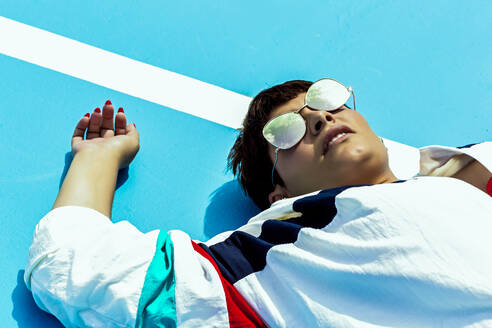 Porträt einer Frau mit verspiegelter Sonnenbrille, die auf dem Boden liegt - ERRF03410
