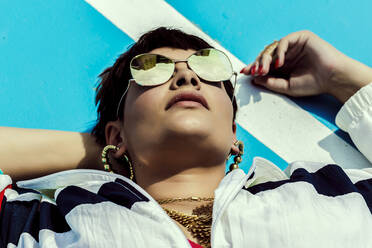 Portrait of woman wearing mirrored sunglasses and lying on ground - ERRF03411