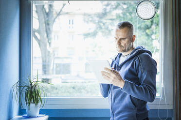 Man using digital tablet near window at home - MCVF00285