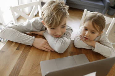 Bruder und Schwester schauen gemeinsam zu Hause auf den Laptop - KMKF01273