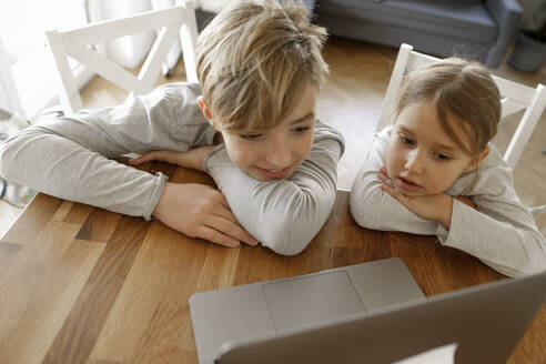 Bruder und Schwester schauen gemeinsam zu Hause auf den Laptop - KMKF01273