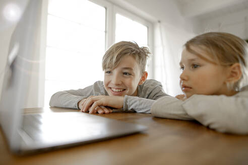 Glücklicher Bruder und glückliche Schwester, die gemeinsam zu Hause auf den Laptop schauen - KMKF01275