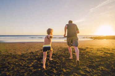 Vater und Sohn laufen am Strand, Rückansicht - IHF00327