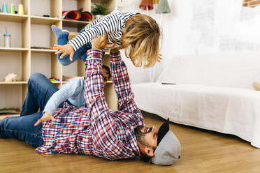 Father lying on floor, holding daughter aloft, pretending to fly - JRFF04323