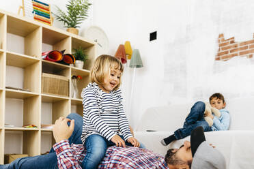 Daughter sitting on top of her father who is lying on the floor, playing at home - JRFF04324