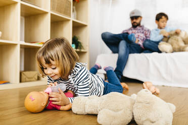 Kleines Mädchen füttert ihre Puppe, während Bruder und Vater auf der Couch sitzen - JRFF04326