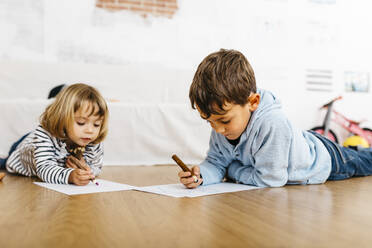 Brother and sister lying on floor of the playroom, drawing on paper - JRFF04327