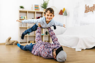Father lying on floor, holding son aloft, pretending to fly - JRFF04335