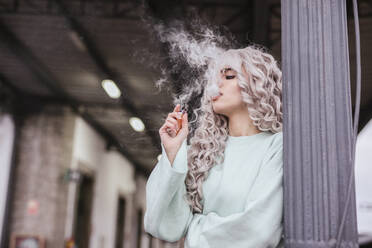 Young woman smoking electronic cigarette on platform - LJF01497