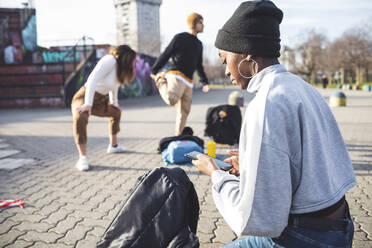 Junge Tänzerinnen und Tänzer proben in einem Skaterpark, junge Frau benutzt Smartphone - MEUF00380