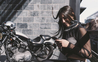 Young woman using smarphone, next to her motor bike - DAMF00336