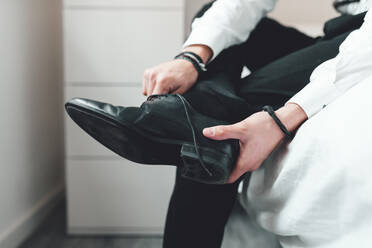 Young man putting on shoes, sitting on bed - AMAF00032