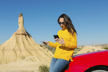 Frau schaut auf ihr Handy in der Wüstenlandschaft von Bardenas Reales, Arguedas, Navarra, Spanien - XLGF00001