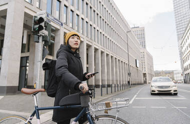Frau mit Fahrrad und Smartphone in der Stadt, Frankfurt, Deutschland - AHSF02210