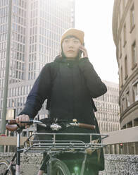 Frau mit Fahrrad beim Telefonieren in der Stadt, Frankfurt, Deutschland - AHSF02215