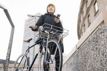 Frau mit Fahrrad und Smartphone in der Stadt, Frankfurt, Deutschland - AHSF02216