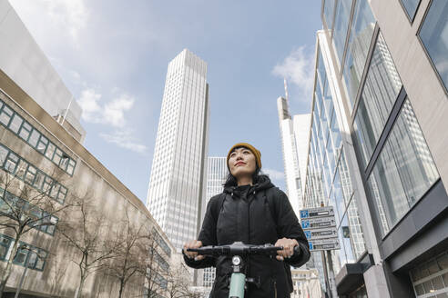 Woman riding scooter in the city, Frankfurt, Germany - AHSF02222