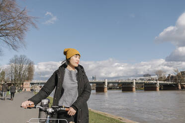 Frau mit Fahrrad am Flussufer, Frankfurt, Deutschland - AHSF02227