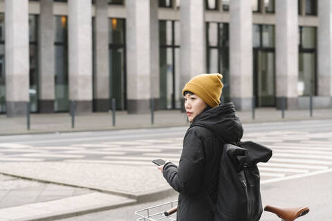 Woman with bicycle and smartphone in the city, Frankfurt, Germany stock photo