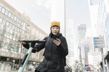 Frau mit Motorroller und Smartphone in der Stadt, Frankfurt, Deutschland - AHSF02245