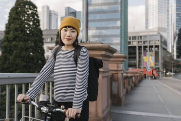 Porträt einer selbstbewussten Frau mit Fahrrad in der Stadt, Frankfurt, Deutschland - AHSF02248