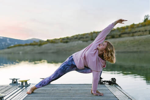 Young woman doing yoga on a jetty, triangle pose - AGGF00001