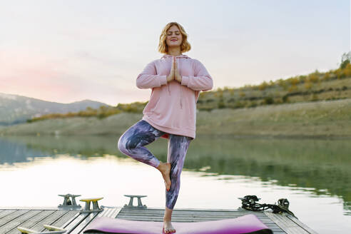 Young woman doing yoga on a jetty, tree position - AGGF00003
