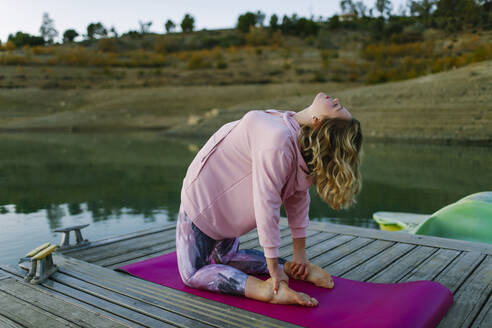 Young woman doing yoga on a jetty, camel pose - AGGF00004